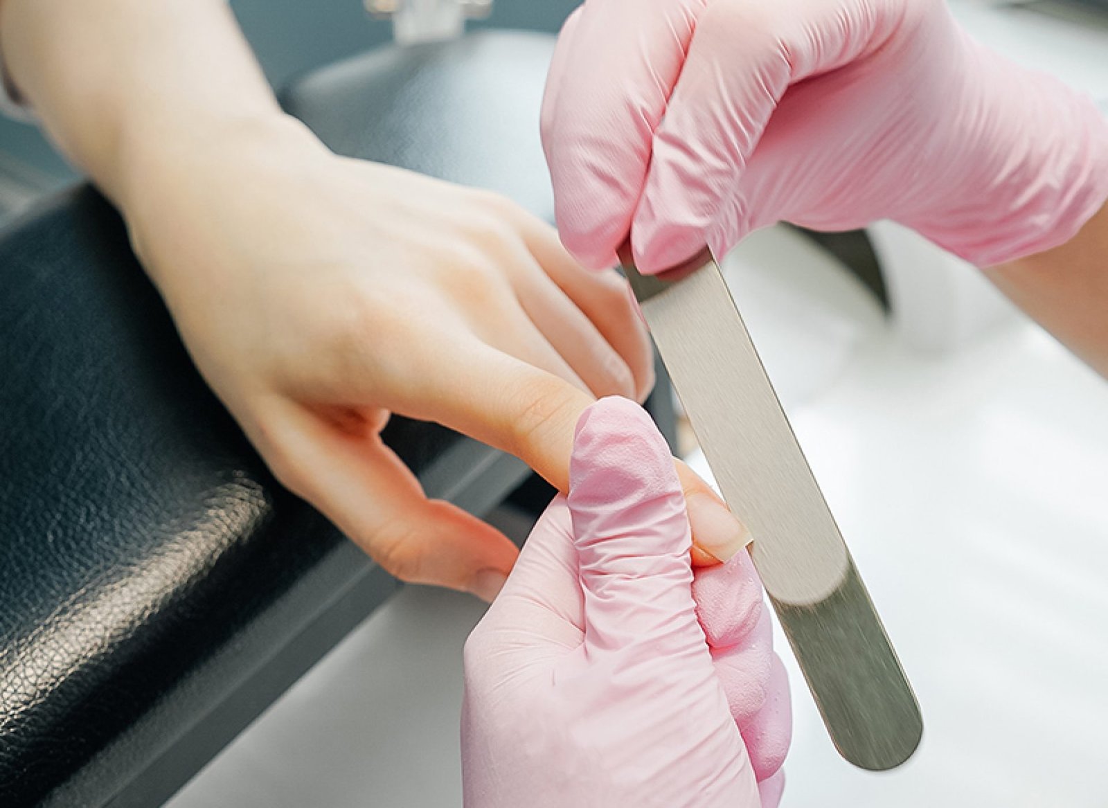 Primer plano de una mano siendo limada por una persona con guantes rosados. La mano está apoyada sobre un soporte negro.